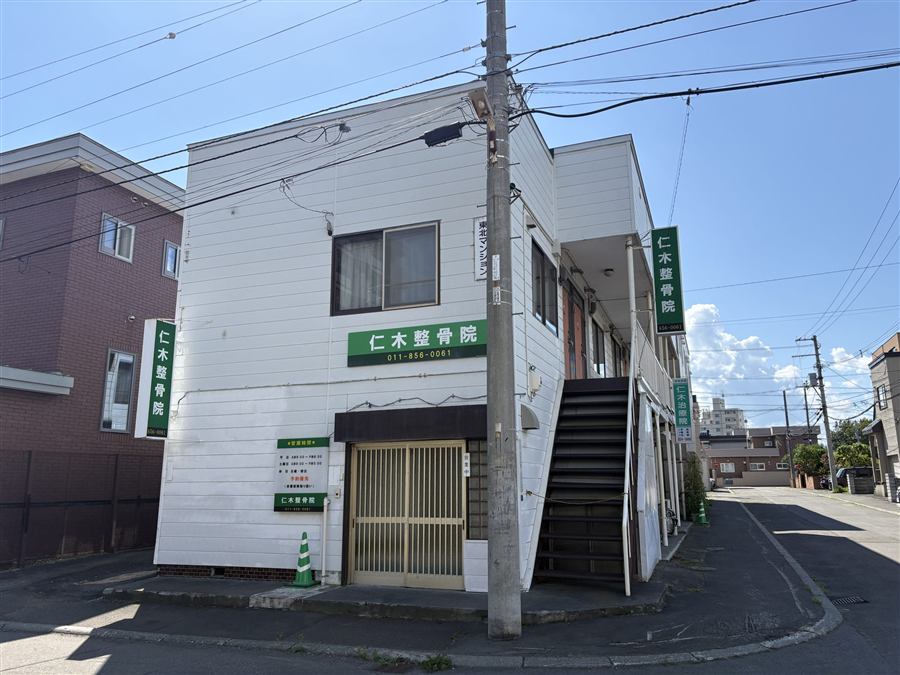 仁木治療院・整骨院の外観。白い外壁の建物で、1階入口に看板が設置されている